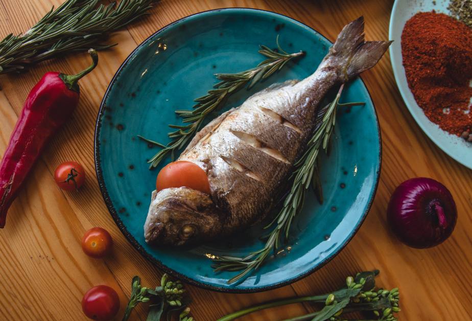 Печена риба с розмарин и зеленчуци върху синя чиния.