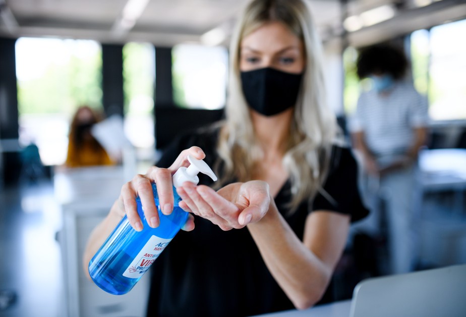 Жена с маска и дезинфектант за ръце в офис.